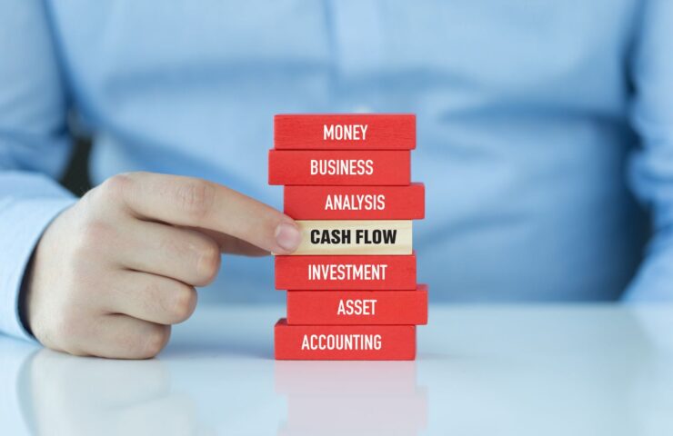 closeup of a man's hand pointing to a stack of red blocks, with one white one in the middle that says, "Cash Flow"