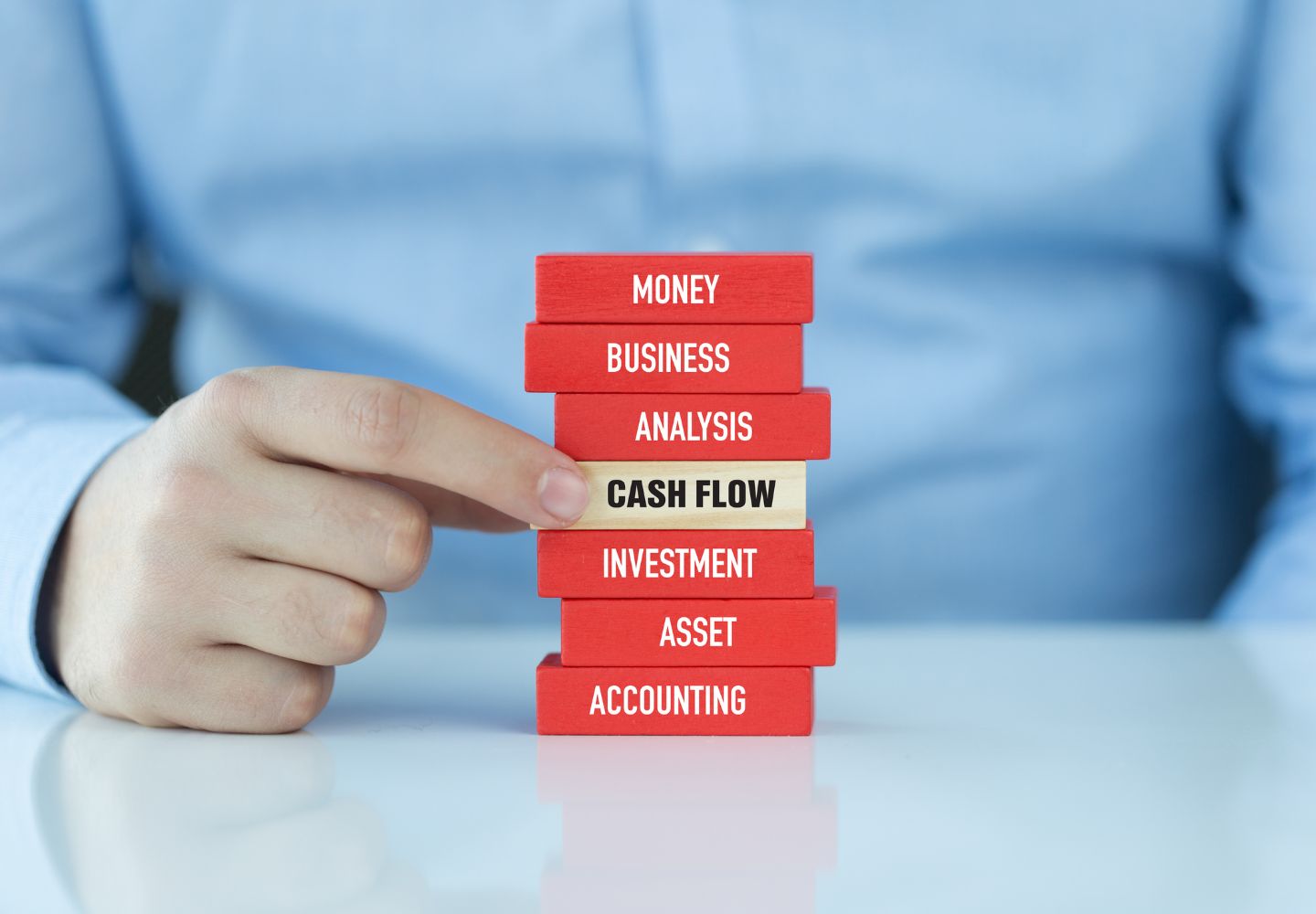 closeup of a man's hand pointing to a stack of red blocks, with one white one in the middle that says, "Cash Flow"