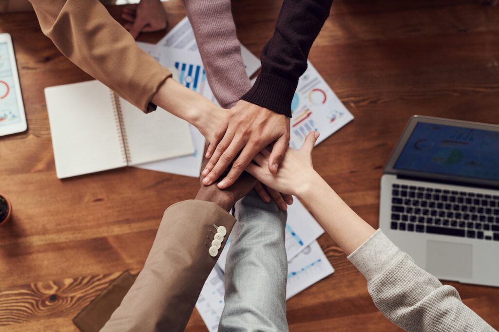 six hands on top of each other above a desk with papers
