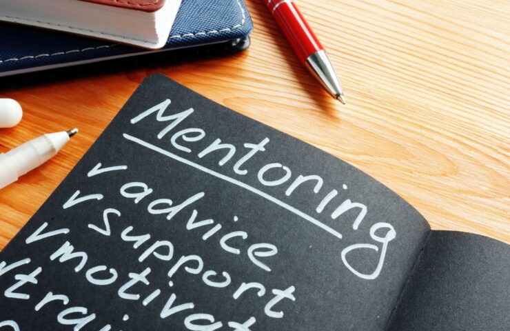 black notebook on a desk with white lettering that says "Mentoring"