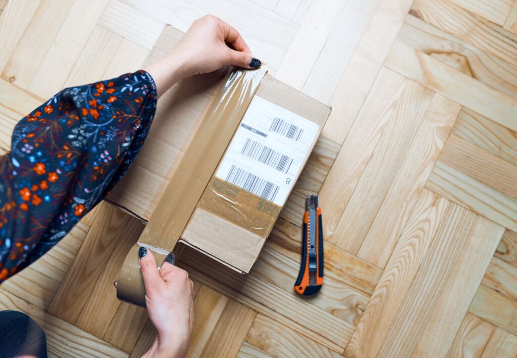 hands putting brown packing tape on a shipping box