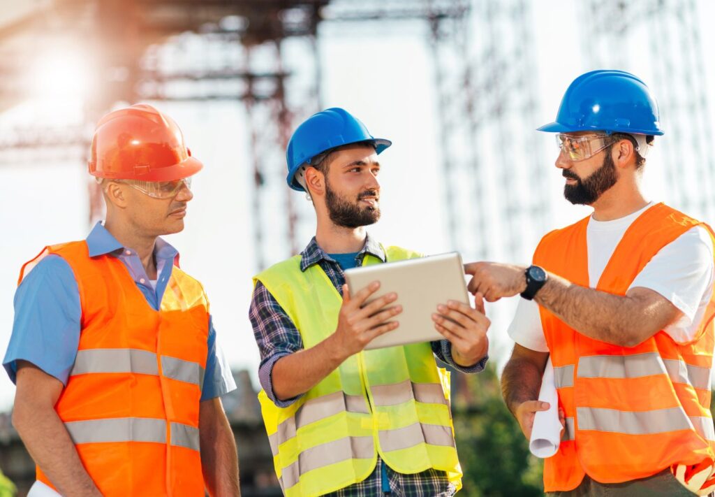 three men with hard hats looking at tablet while at construction site