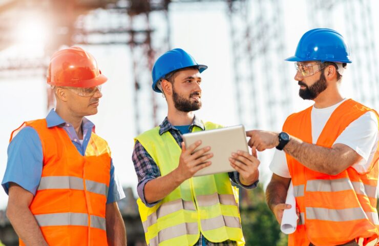 three men with hard hats looking at tablet while at construction site