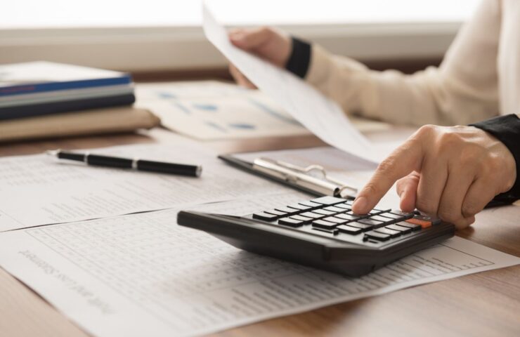 closeup of someone using a calculator on a desk and holding a piece of paper