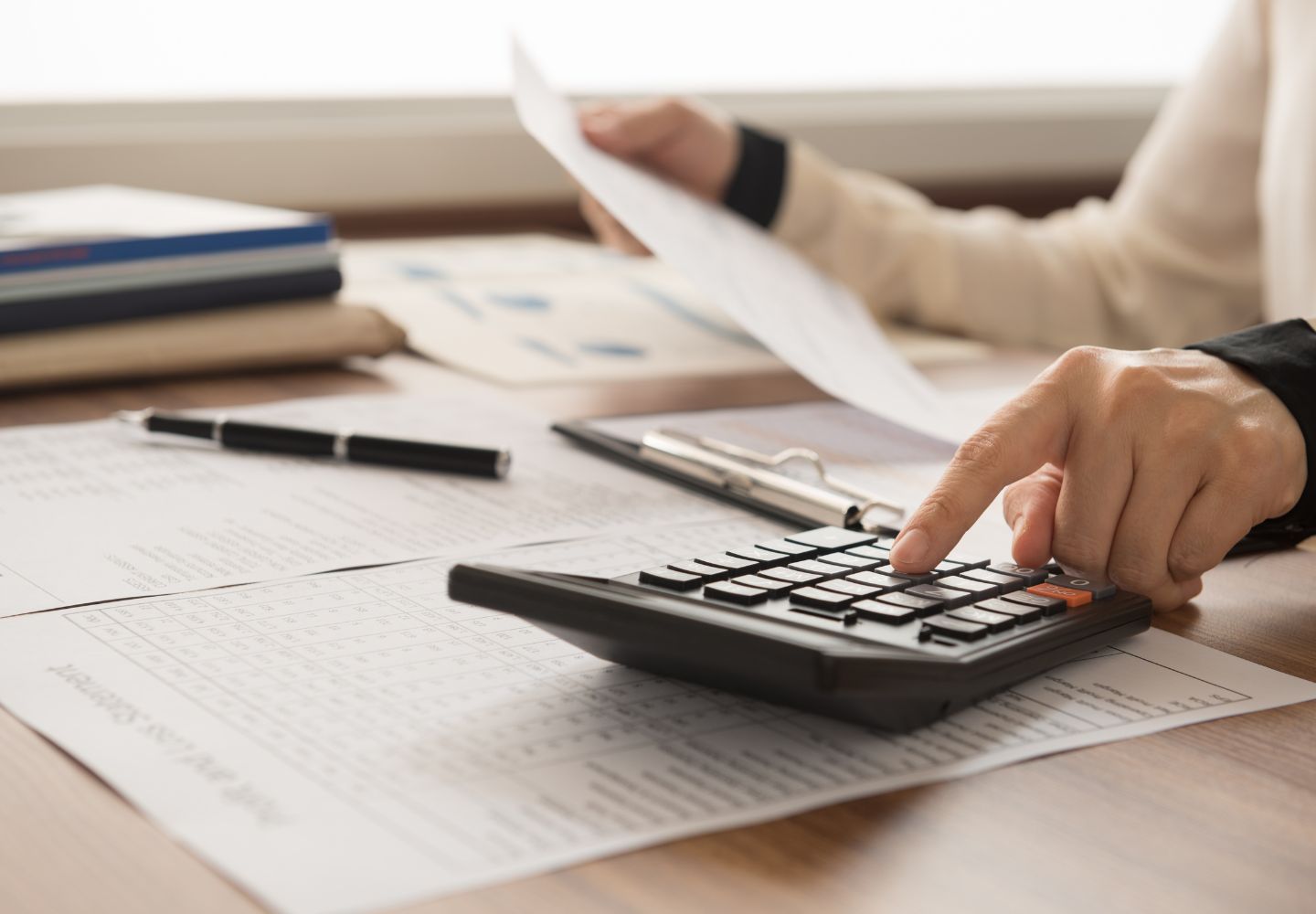 closeup of someone using a calculator on a desk and holding a piece of paper