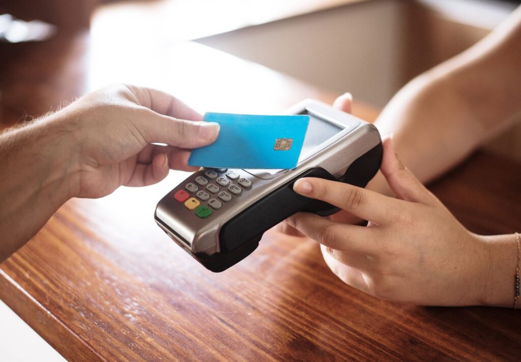 hand holding a blue credit card above a POS machine